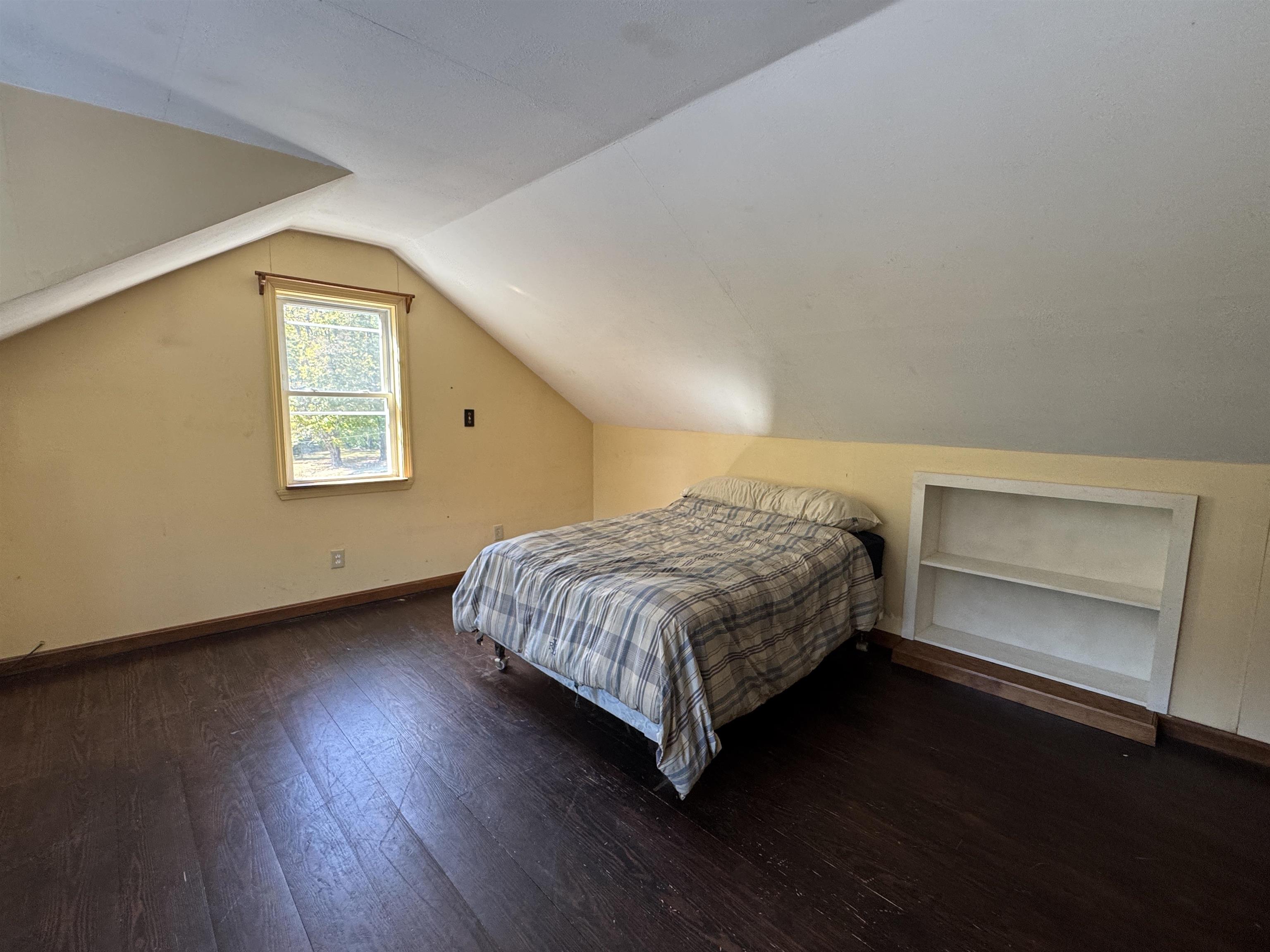 Charming upstairs bedroom with cozy sloped ceilings, natural light, and built-in shelving